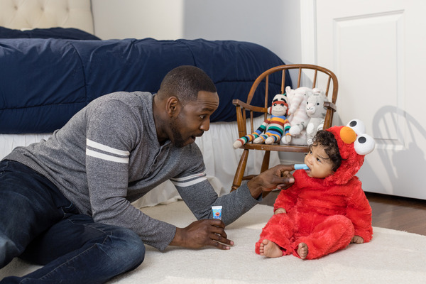 Baby wearing Elmo costume gets her teeth cleaned with Orajel finger brush.